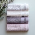 towels are stacked on a table with a vase of flowers